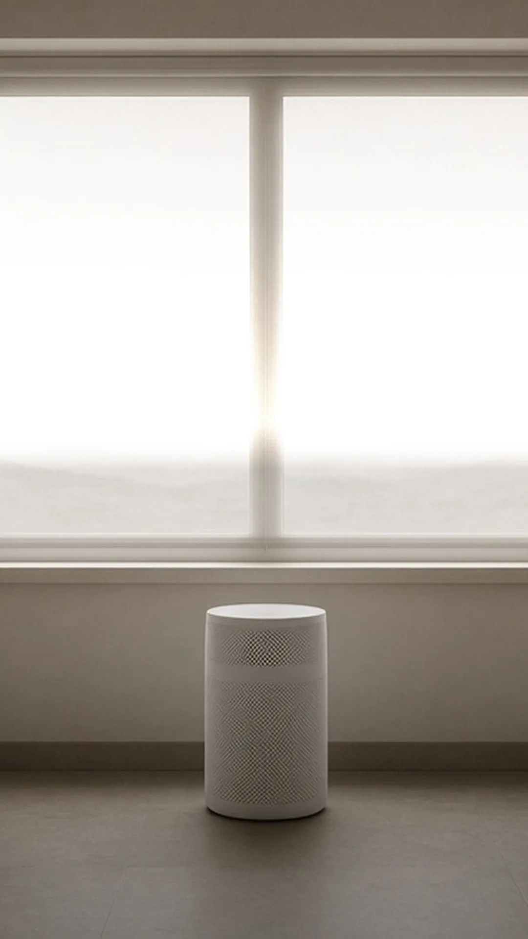 A white cylindrical air purifier below a wide two-pane window looking out on hazy hills