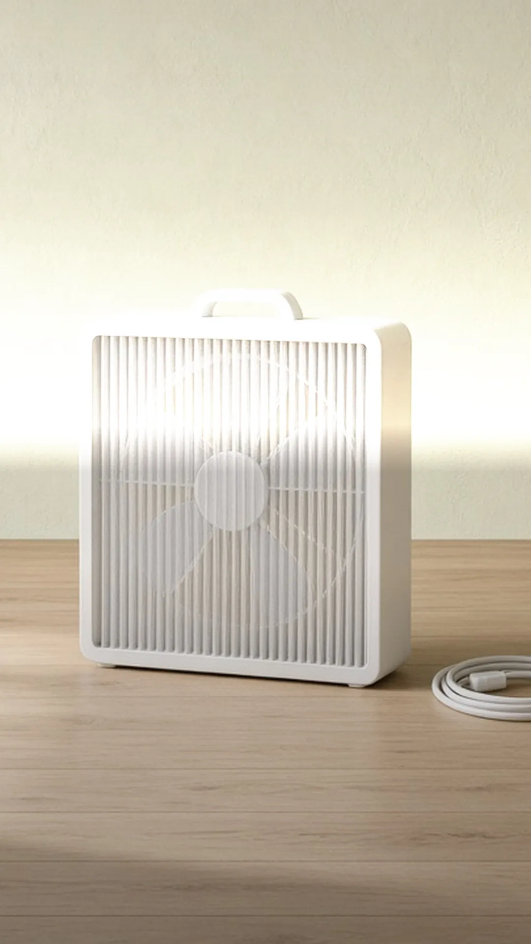 A white box fan with a pleated filter panel across its front, blades faintly behind it, unplugged, cord coiled on light oak
